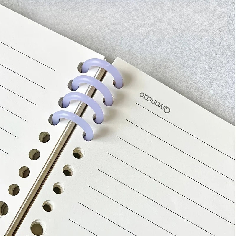 A close-up of a spiral notebook showing purple plastic binding rings and ruled paper.