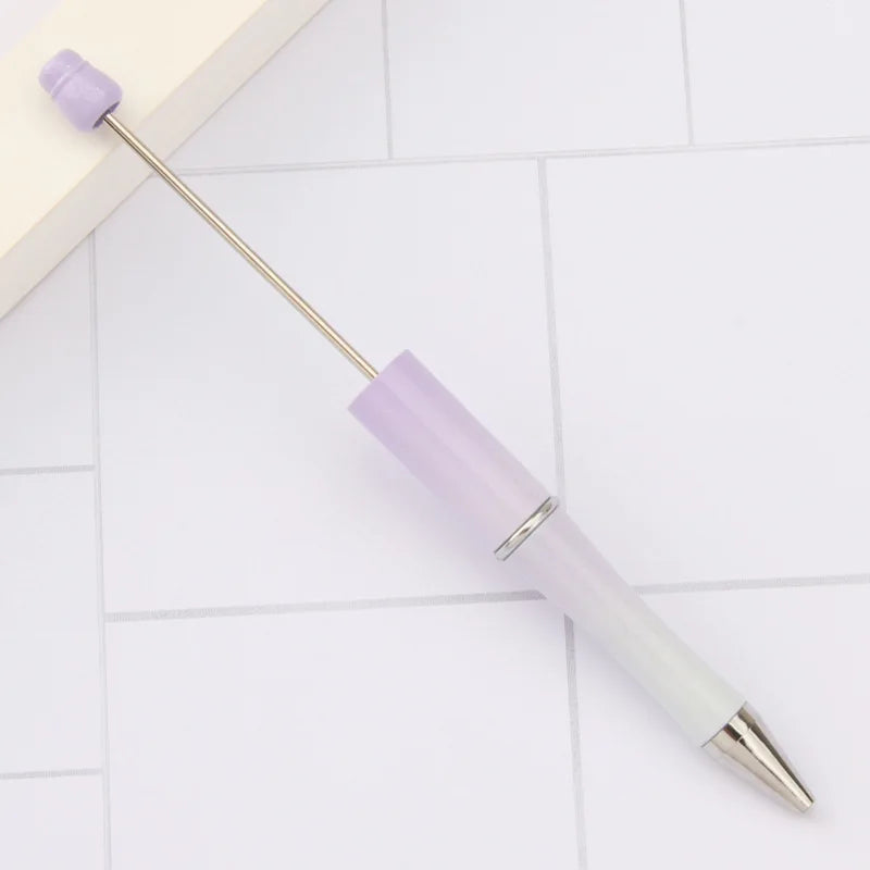 A purple and white DIY beadable pen set with a gold-tipped applicator resting on a light surface.