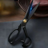 A pair of professional stainless steel tailor scissors with a gold accent, lying on a dark surface.