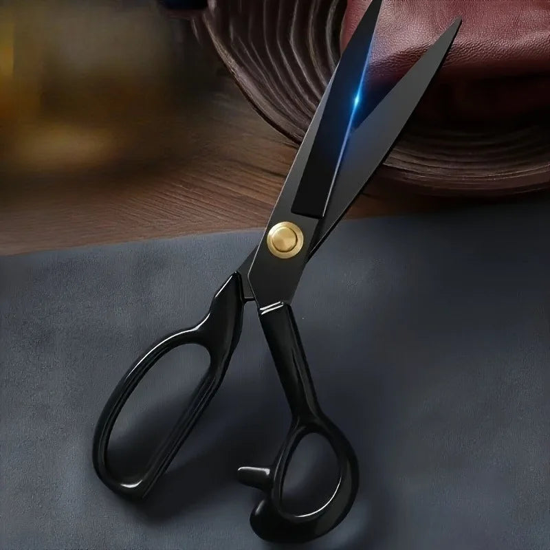 A pair of professional stainless steel tailor scissors with a gold accent, lying on a dark surface.