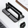 A black vertical laptop stand designed to hold a MacBook or tablet, shown next to a laptop keyboard.