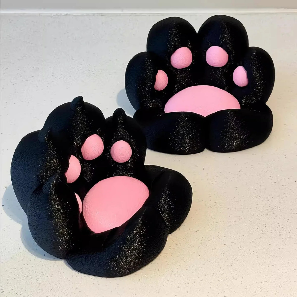 A pair of black, glittery cat paw phone stands with pink pads, shown from above.