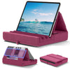 A pink foldable tablet pillow stand with a built-in pocket and a tablet resting on it.