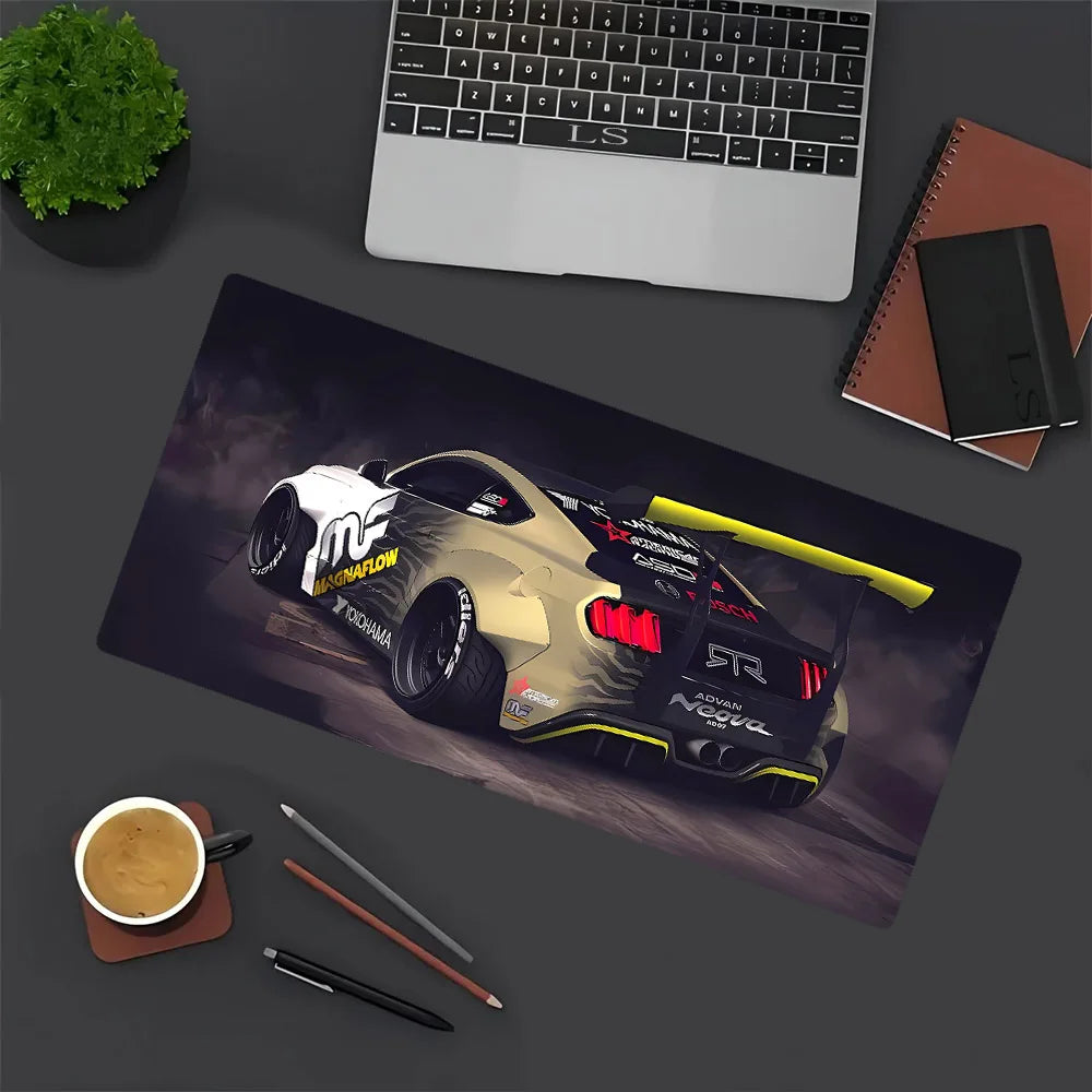 A large gaming mouse pad featuring a detailed JDM car design, placed next to a laptop and writing tools.