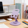 A purple foldable desktop phone stand is shown on a wooden desk next to a laptop and books.