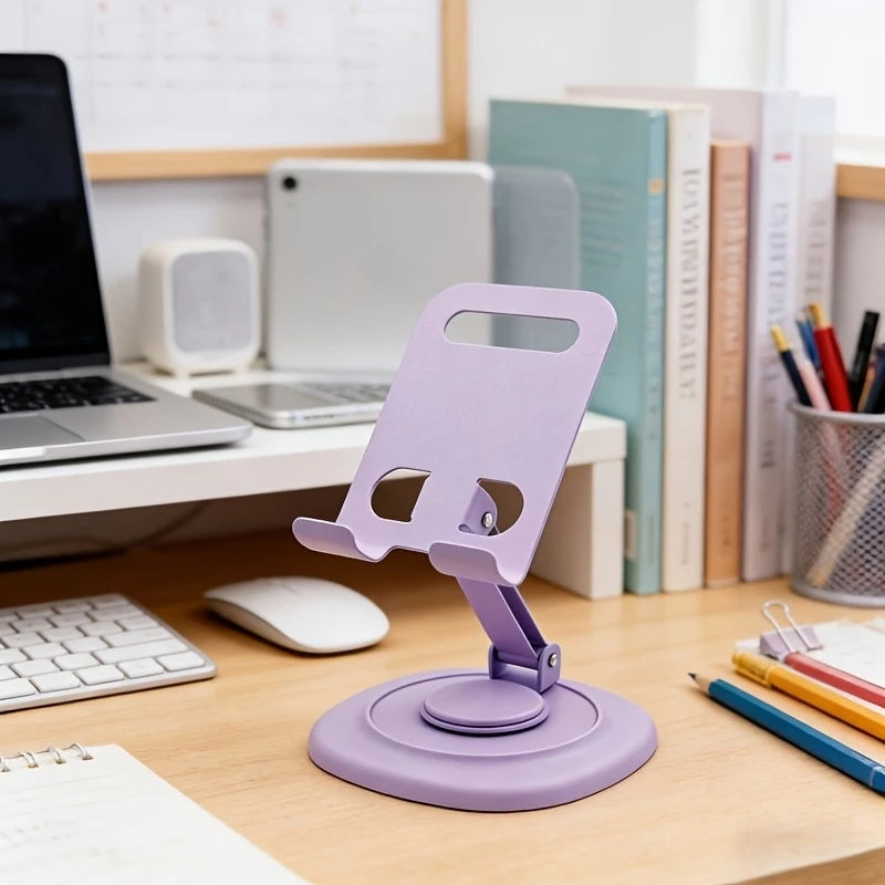 A purple foldable desktop phone stand is shown on a wooden desk next to a laptop and books.
