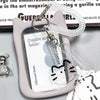 A pink crystal clear card holder with a cat charm keychain is displayed on a dark surface.