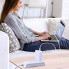 A woman is using a Universal USB-C Power Adapter for Laptops to charge a laptop on a couch.