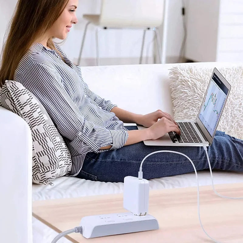 A woman is using a Universal USB-C Power Adapter for Laptops to charge a laptop on a couch.