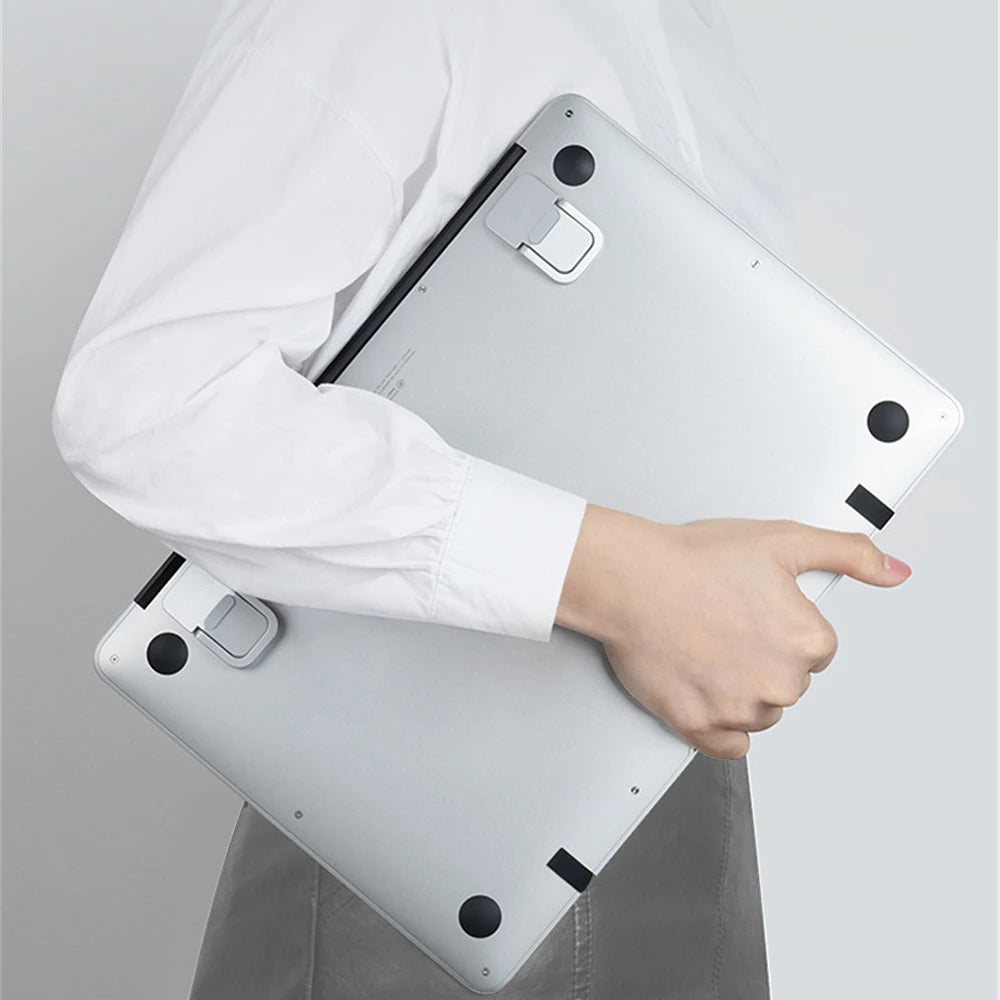 Una persona sostiene un soporte portátil de laptop de aluminio plateado, mostrando su diseño y características.
