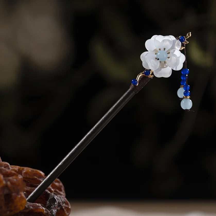 Une délicate épingle à cheveux en bois avec un charm floral blanc et des perles bleues.