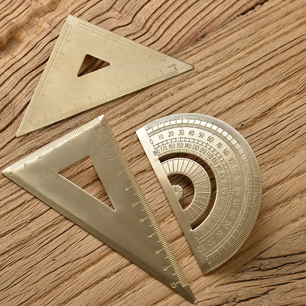 A set of retro brass triangle rulers and a circular graduated ruler resting on a wooden surface.