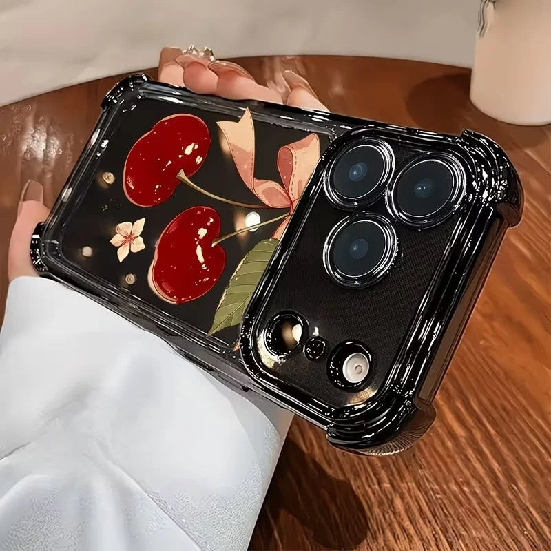 A black iPhone case with a cherry bow pattern and electroplated finish is held by a person on a wooden surface.