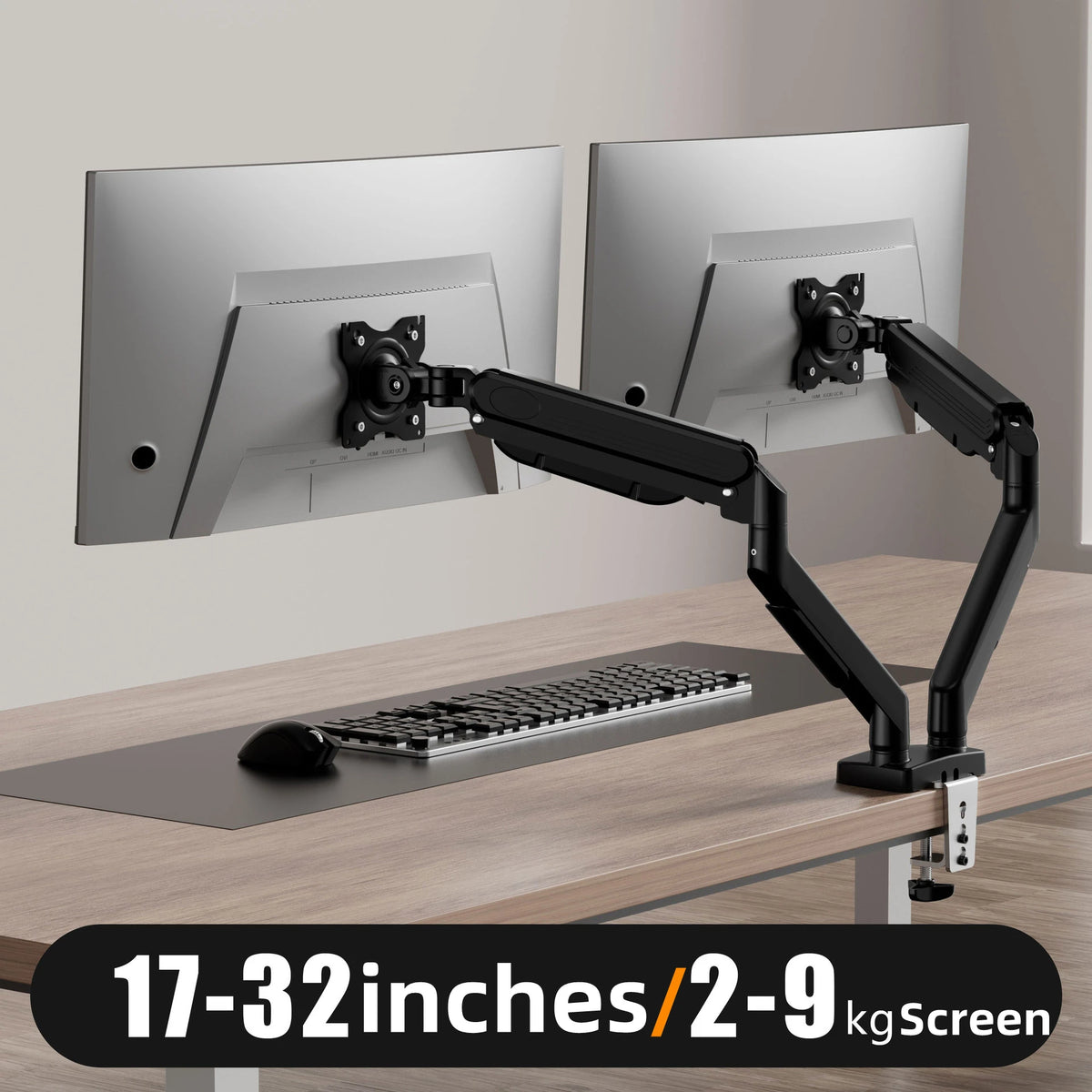A black ergonomic dual monitor mount is shown adjusting a silver monitor on a wooden desk.