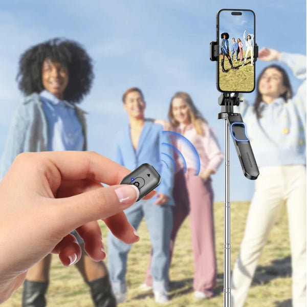 A hand holds a black multifunctional selfie stick tripod with a Bluetooth remote, set against a background of people outdoors