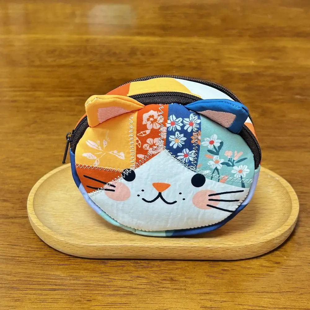 A colorful patchwork cat face coin purse with a zipper, featuring orange, blue, and white floral patterns.