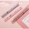 A pink plastic measuring tool with a cat paw design is shown next to a pink notebook.