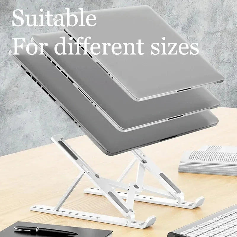 A silver foldable adjustable laptop stand is shown with a laptop resting on it, next to a keyboard and pen.