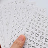 A hand holds a sheet of metallic 3D star nail art stickers, showing various heart and star shapes.