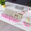 Un ensemble de trois repose-poignets en forme de nuage rose et un clavier mécanique argenté sur une surface de marbre blanc.
