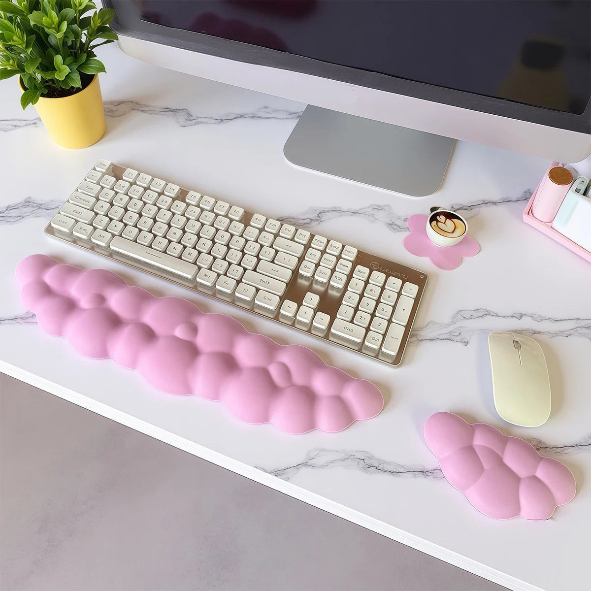 Un ensemble de trois repose-poignets en forme de nuage rose et un clavier mécanique argenté sur une surface de marbre blanc.