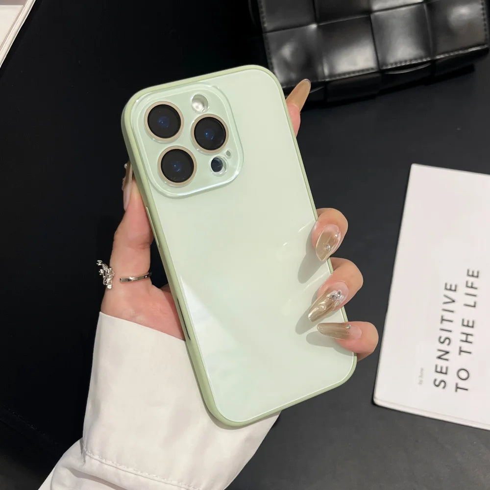 A hand holds a light green iPhone with a clear case and gold nail polish against a black background.
