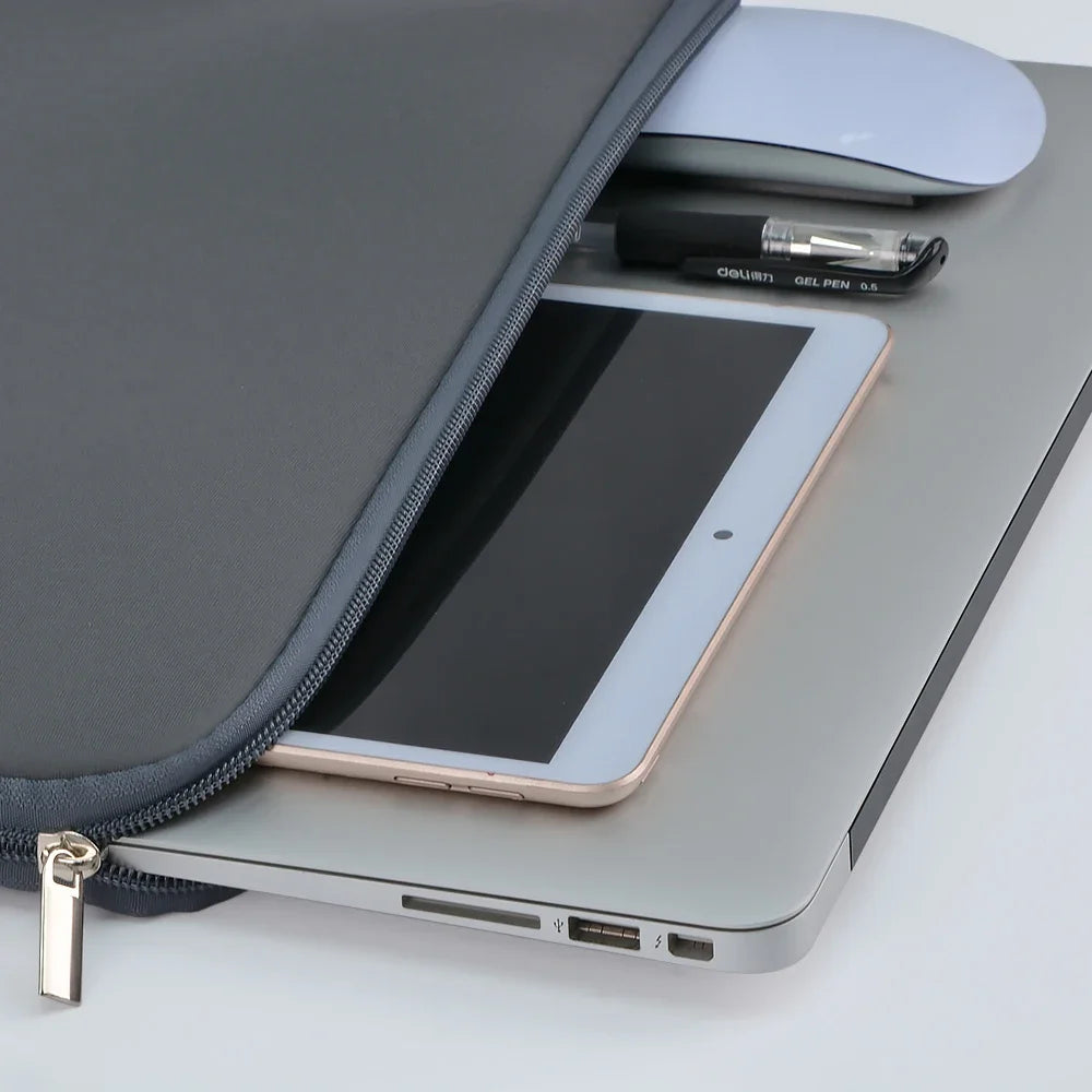 Una funda plateada para portátil abierta, mostrando una tableta dentro con un lápiz óptico y un ratón cerca.