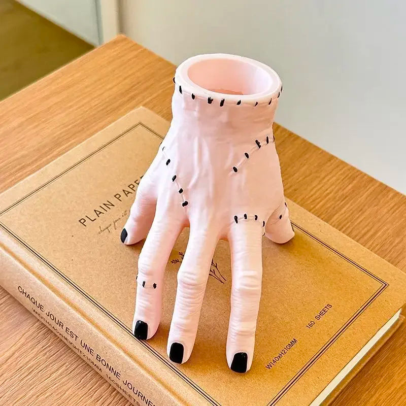Pink resin palm hand decoration with black accents resting on a brown book.