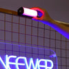 A hand holds a magnetic RGB handheld light wand illuminating a grid background with neon text.