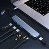 A silver multi-port USB-C hub adapter with multiple ports and an audio jack is shown next to a laptop keyboard.