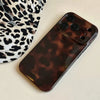 A dark brown leopard print phone case for an iPhone resting on a light surface next to a patterned fabric.