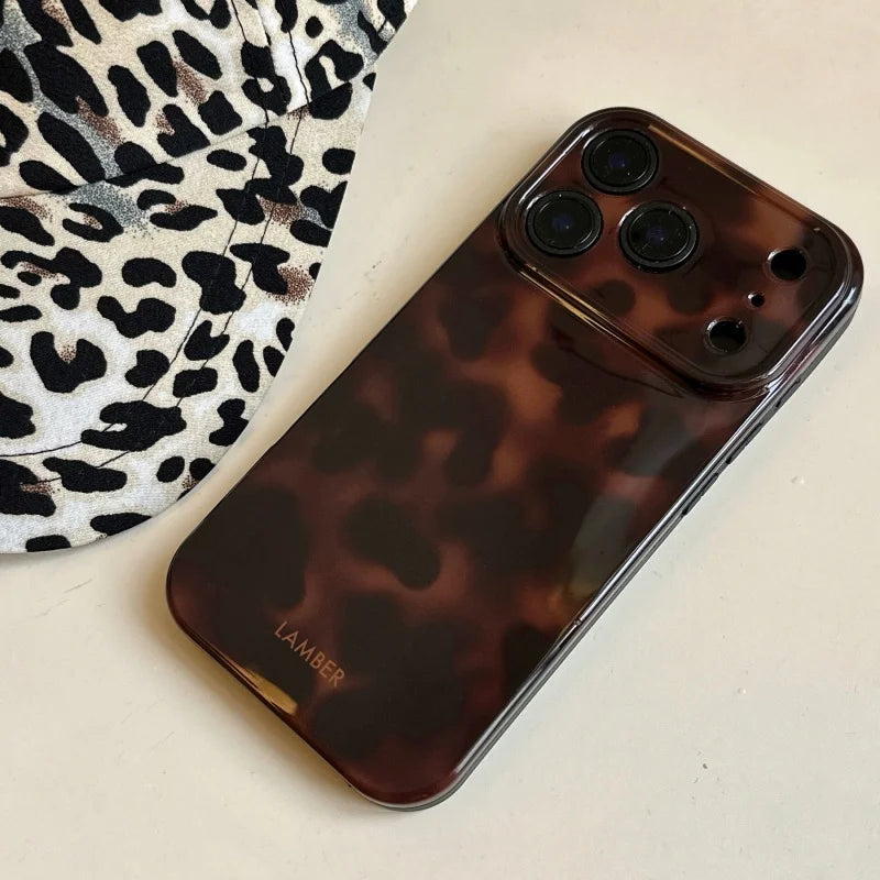 A dark brown leopard print phone case for an iPhone resting on a light surface next to a patterned fabric.