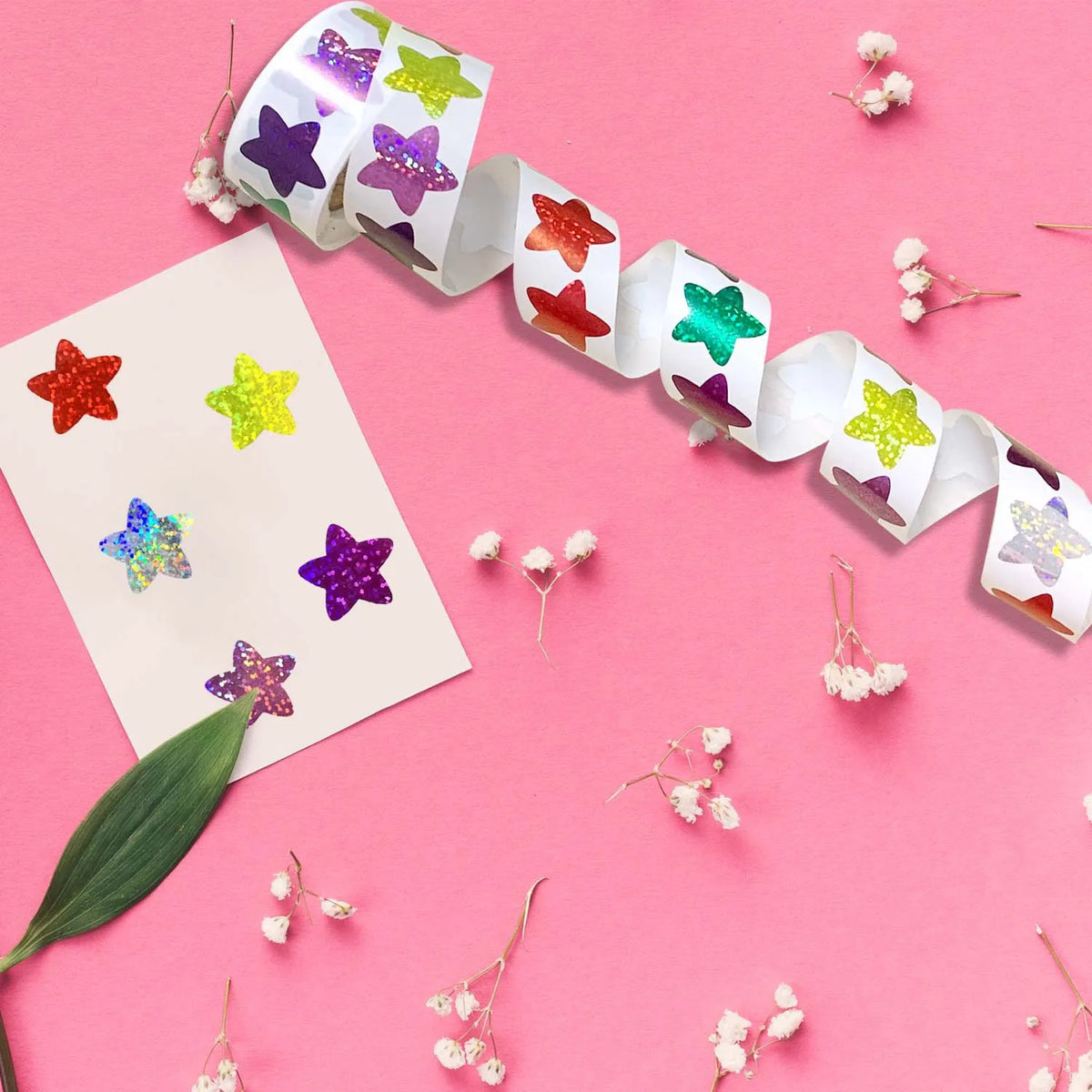 Eine Rolle Glitzer-Stern-Sticker in verschiedenen Farben wird auf einem rosa Hintergrund mit kleinen weißen Blumen präsentier