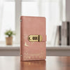 A pink leather personal finance budget binder with a brass lock detail resting on a wooden surface.