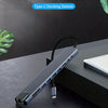 A compact Type-C docking station with a black cable is shown resting on a dark surface next to a laptop.