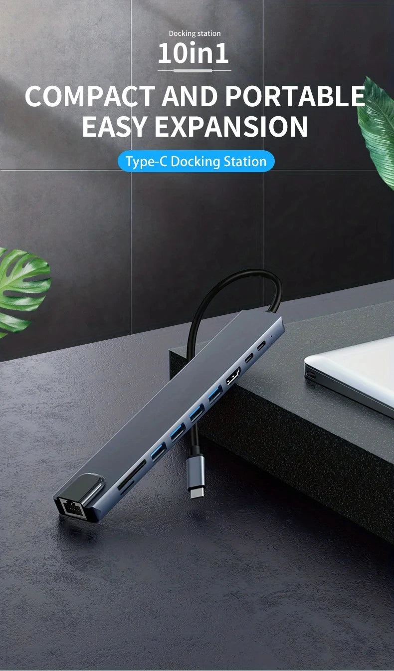 A compact Type-C docking station with a black cable is shown resting on a dark surface next to a laptop.