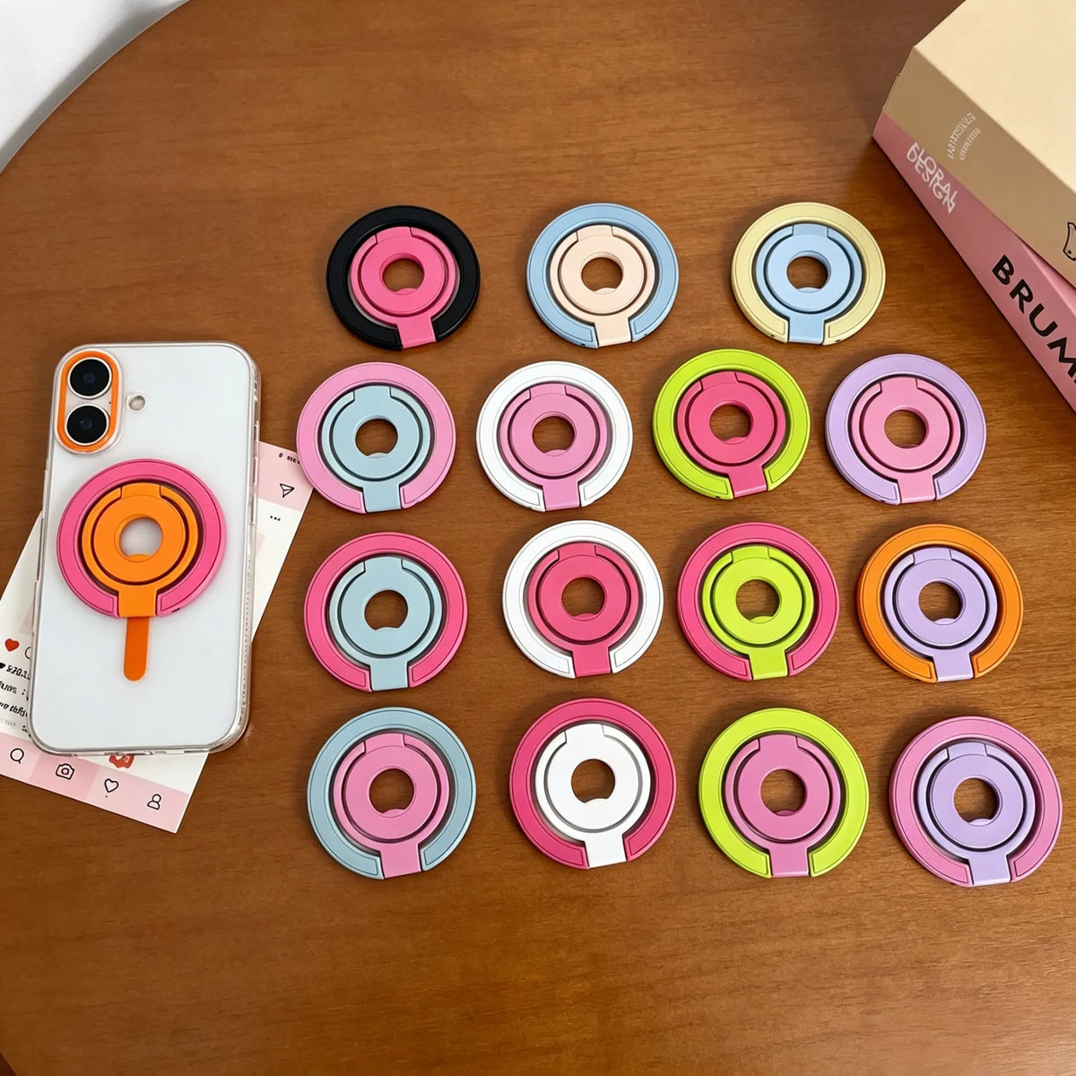 A collection of colorful magnetic phone grips and stands with foldable rings arranged on a wooden surface.