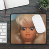 A close-up photo of a blonde cartoon doll head with large eyes and pink lips placed on a black mouse pad.