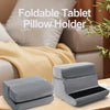 A gray foldable tablet pillow holder is shown resting on a wooden surface.