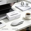 A white rechargeable wireless Bluetooth mouse is shown next to a laptop and a cup on a desk.