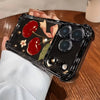 A black iPhone case with a cherry and floral pattern is held by a person on a wooden surface.