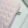 A pink quilted laptop sleeve with a white gingham pattern is shown on a white surface.