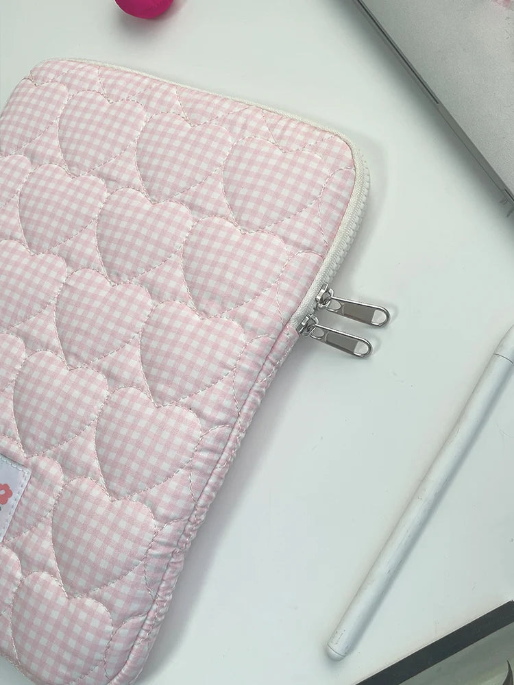 A pink quilted laptop sleeve with a white gingham pattern is shown on a white surface.