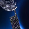 A close-up view of a mechanical RGB wired keyboard attached to a metallic robotic hand, highlighting its ultra-portable desig