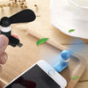 Una mano sostiene un ventilador USB portátil negro junto a un smartphone sobre una tabla de cortar de madera.