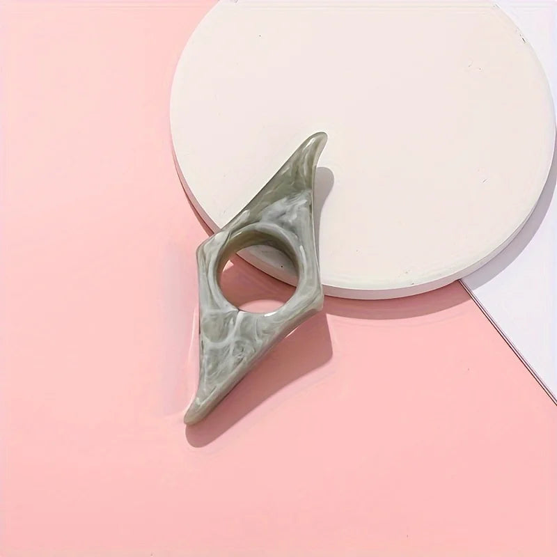 A light green resin thumb book stand resting on a pink surface next to a white circular object.