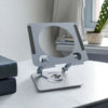 A silver foldable tablet and phone stand with a circular cutout for viewing, resting on a white surface.