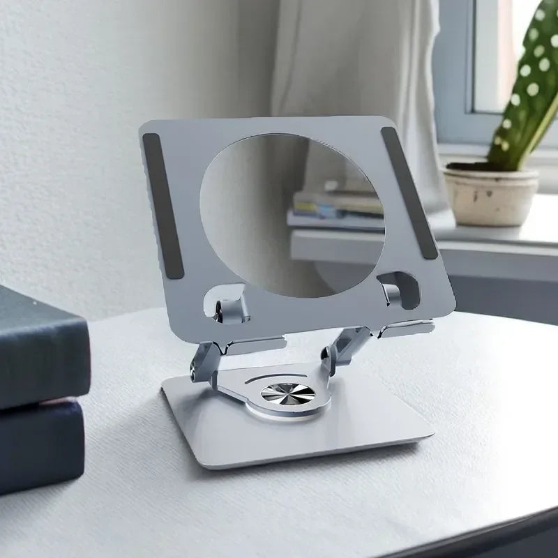 A silver foldable tablet and phone stand with a circular cutout for viewing, resting on a white surface.