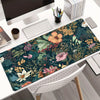 A large floral design mouse pad with a dark green background and various earthy tones is placed on a white desk.