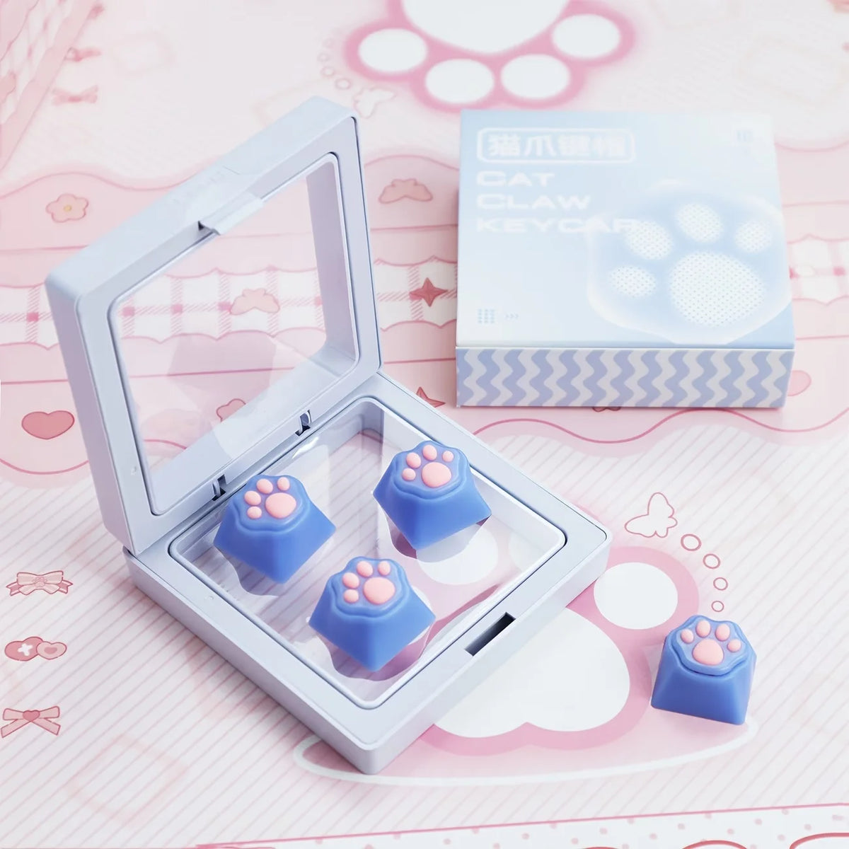 A clear plastic case containing blue cat claw keycaps and a box labeled Cat Claw Keycaps for MX Switches on a pink background